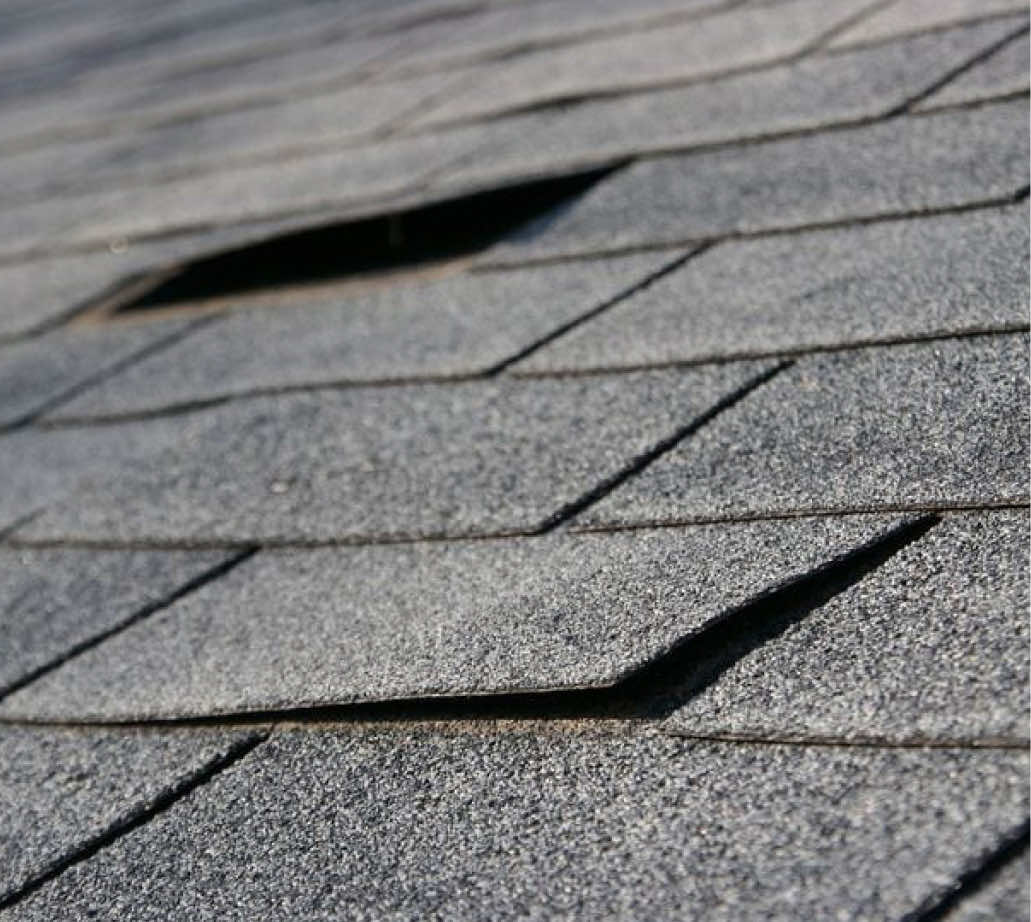 Close-up view of damaged roof shingles showing cracks and gaps.