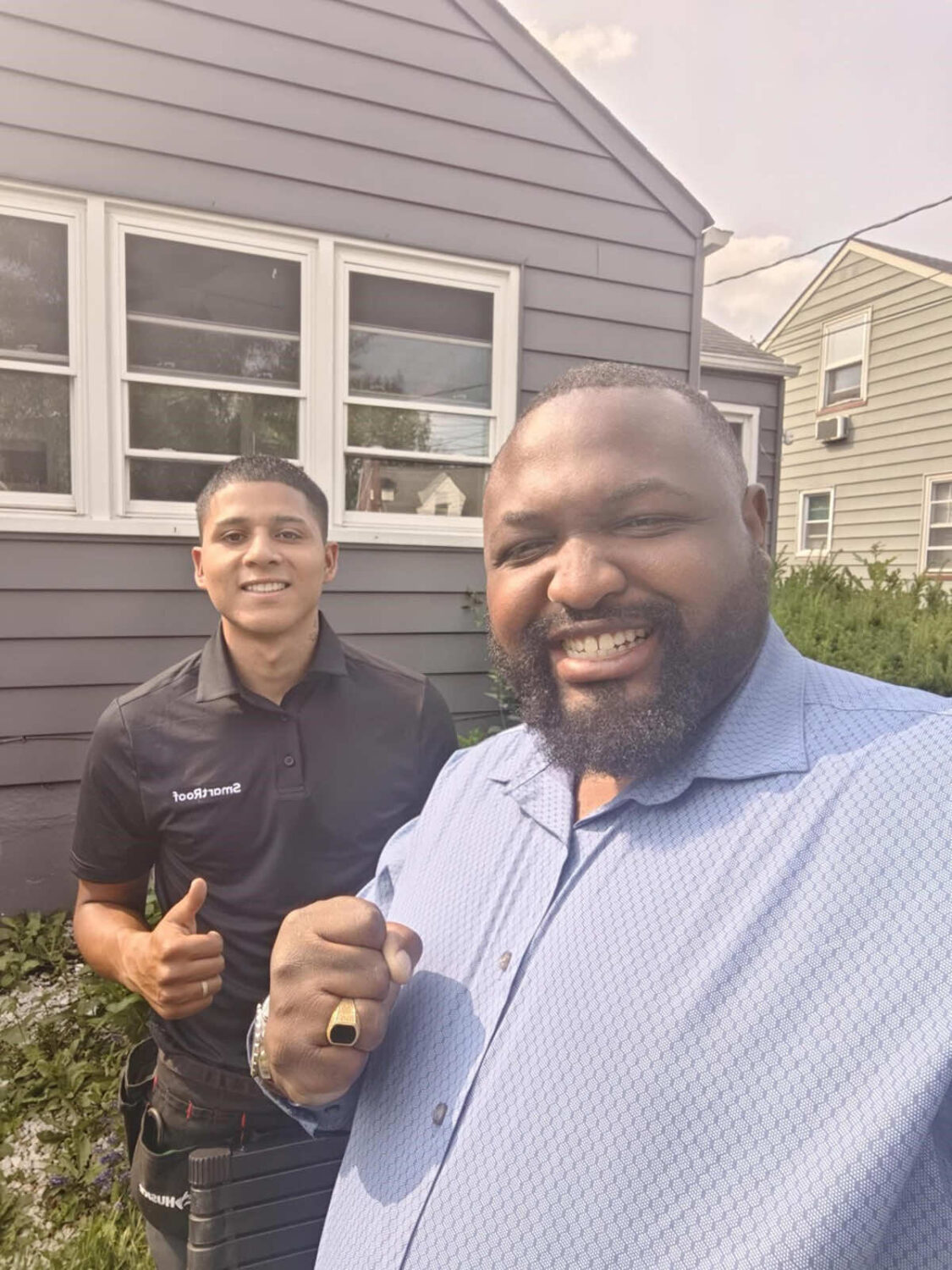 Two team members smiling together in front of a house showing thumbs up