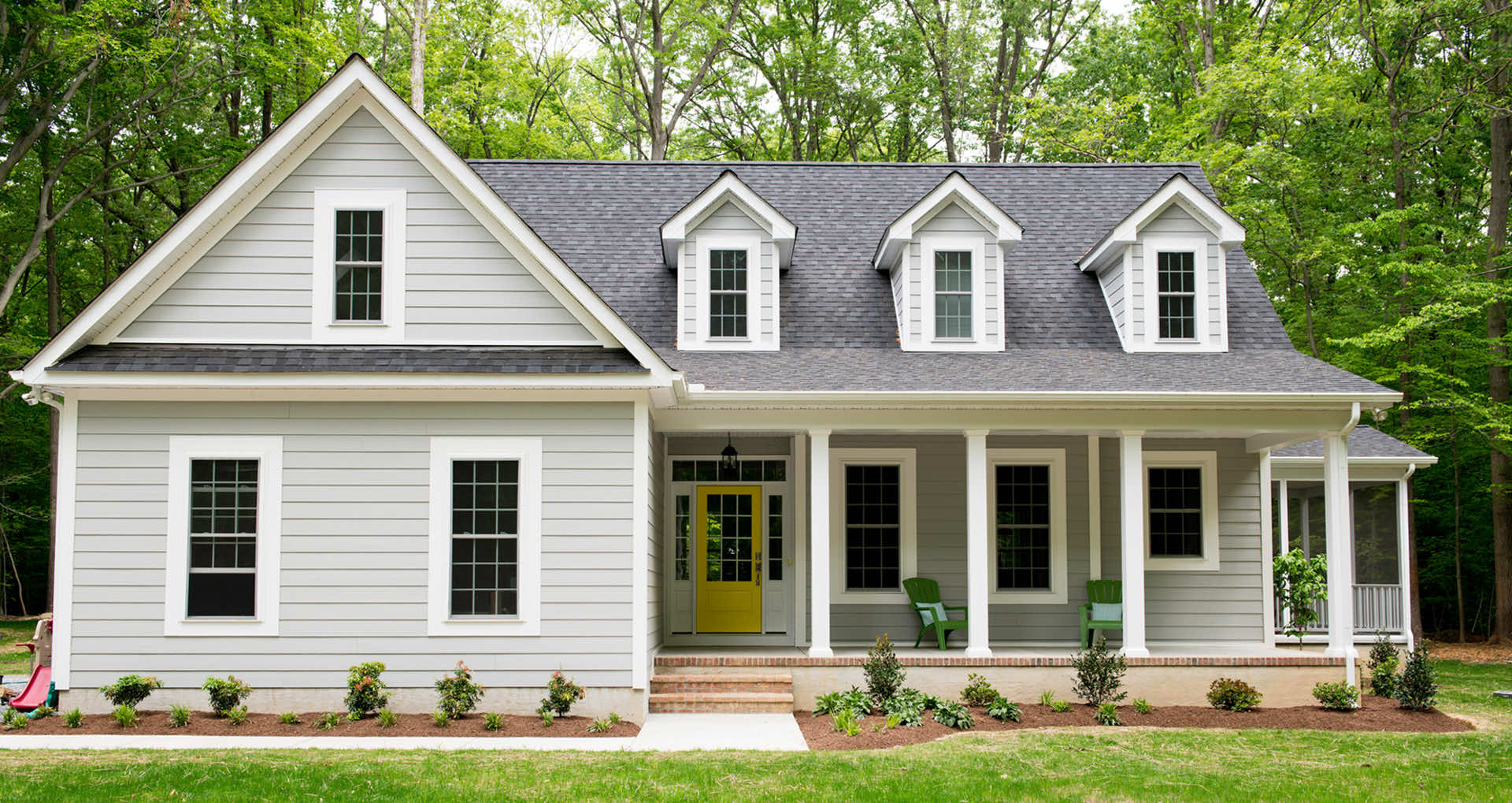 Modern grey house with a yellow front door surrounded by greenery