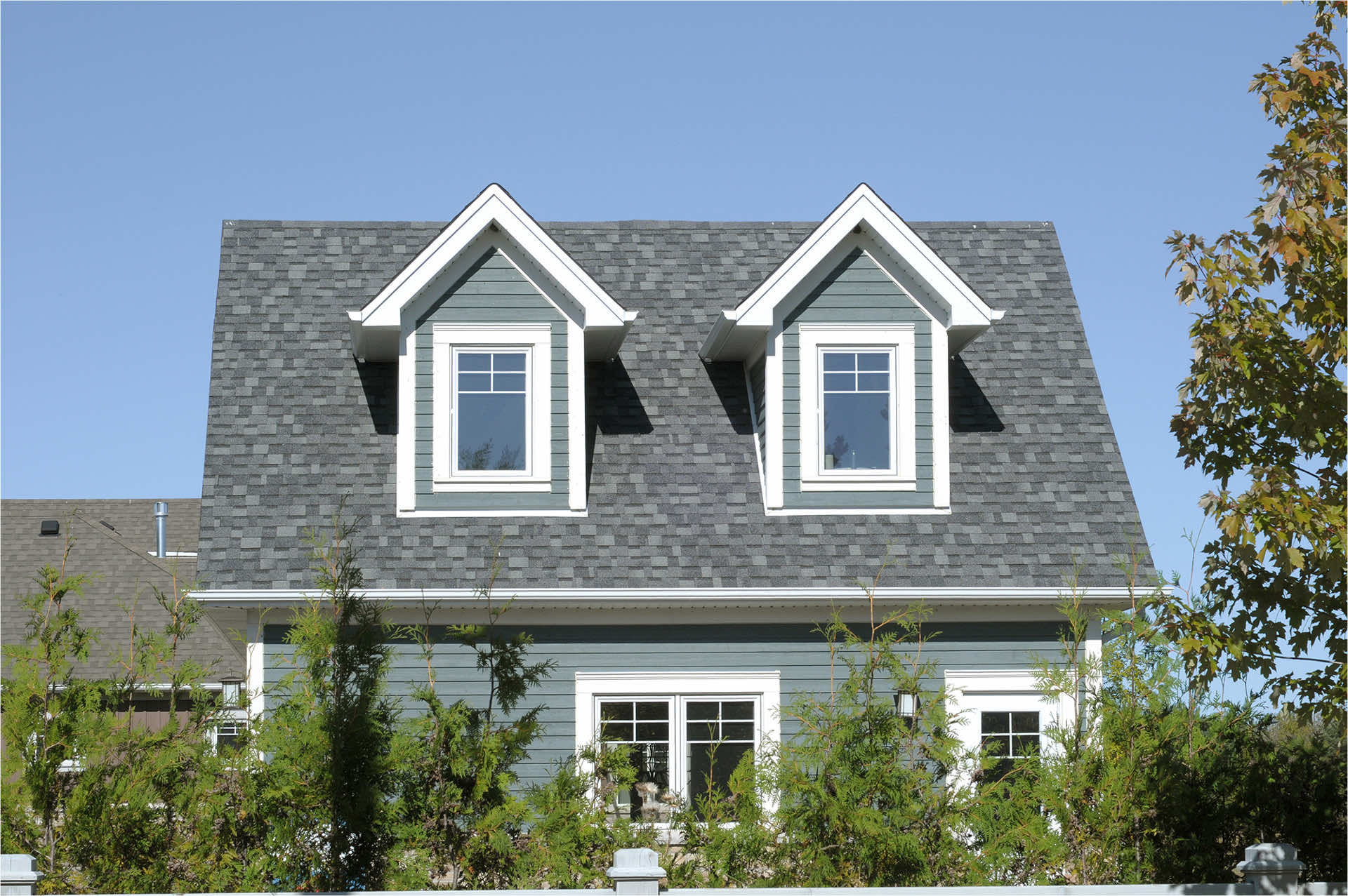 A close-up view of a residential house featuring a gray roof and gable windows under a clear blue sky