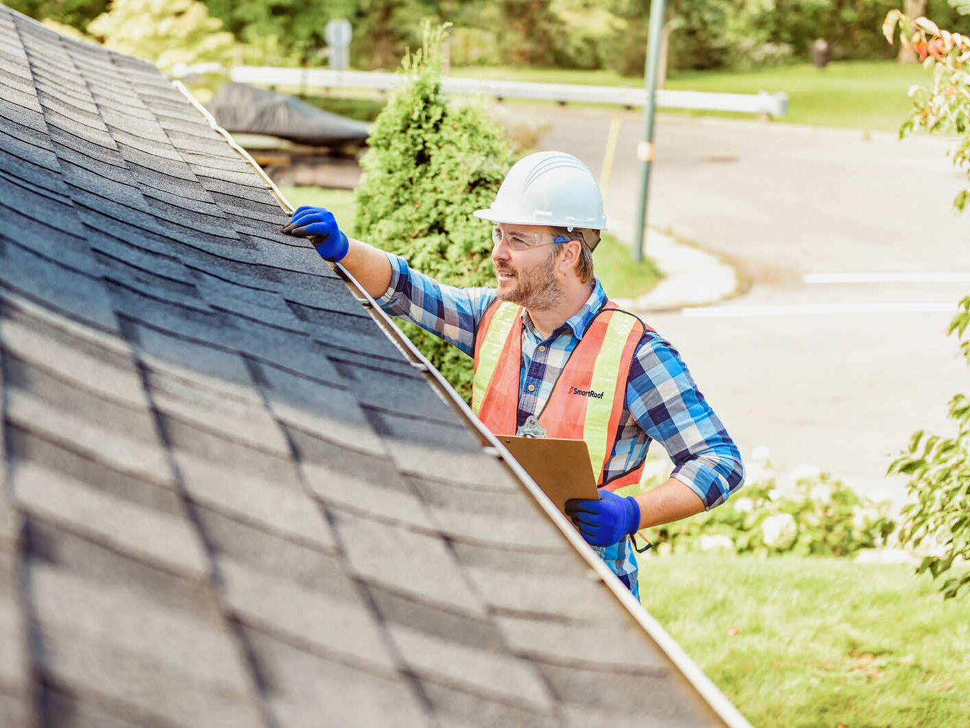 A roofing worker inspecting shingles on a sloped roof with a clipboard.