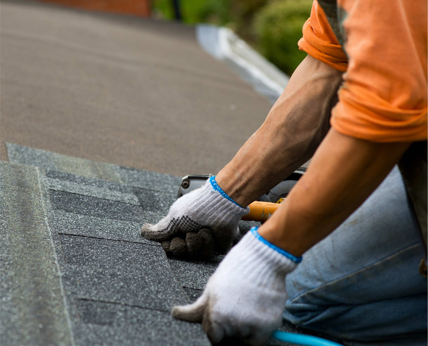 A close-up of a worker installing roofing shingles with gloved hands on a residential roof.