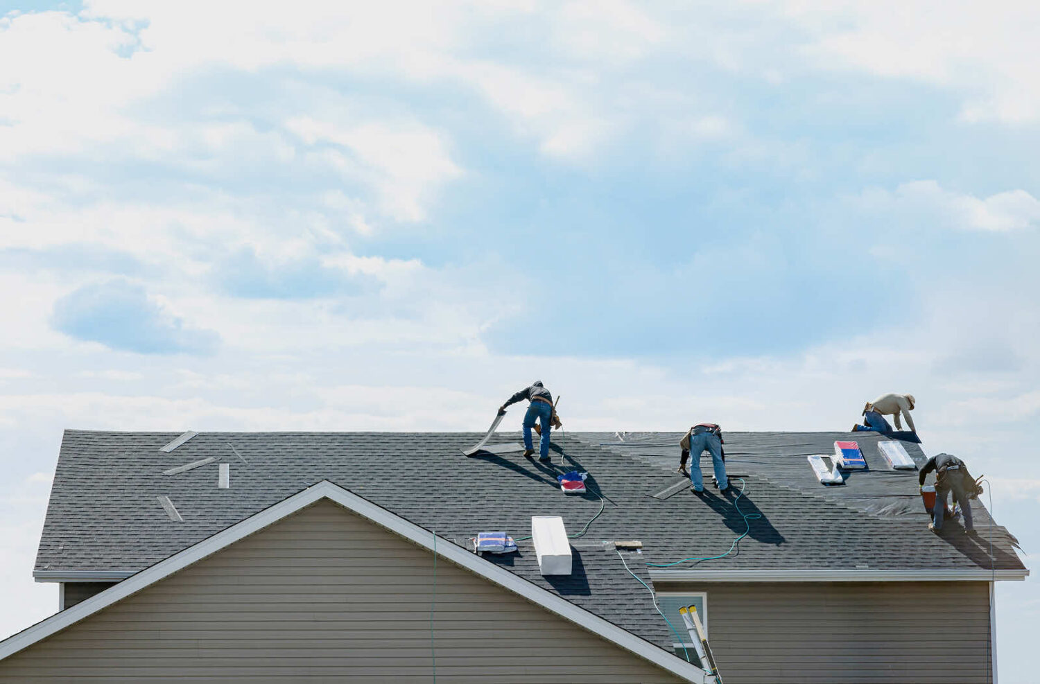 A team of roofers working on a home installation under a blue sky.