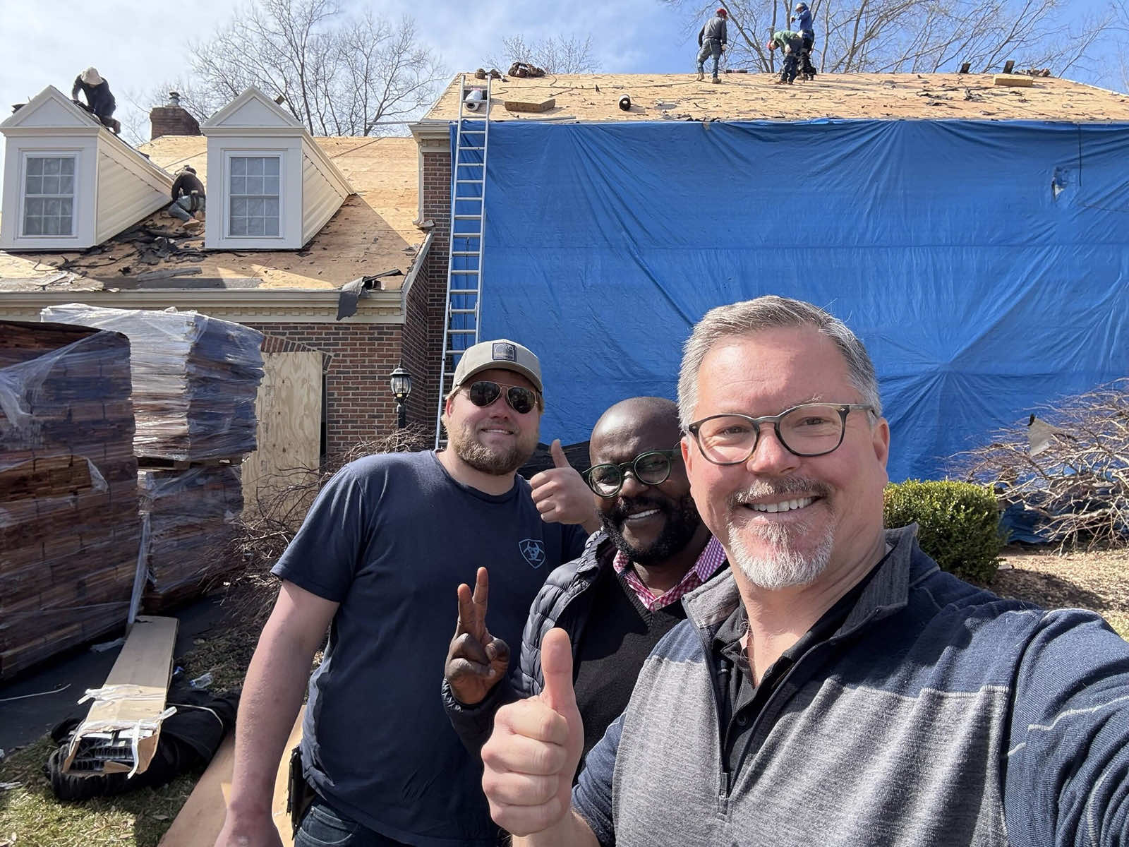 Team members taking a selfie in front of a roofing project with work in progress on the roof