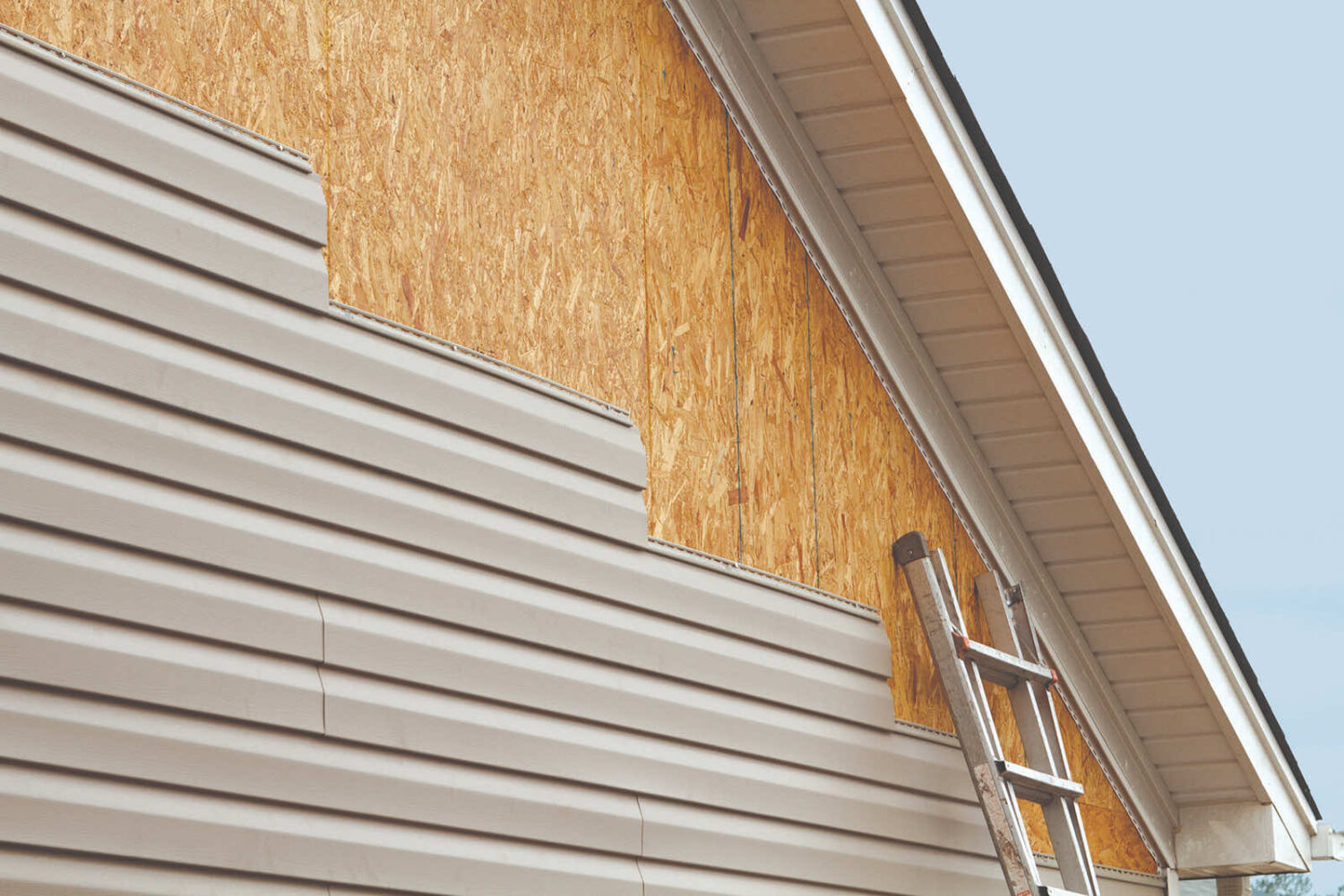 Close-up of siding being repaired with a ladder in view.