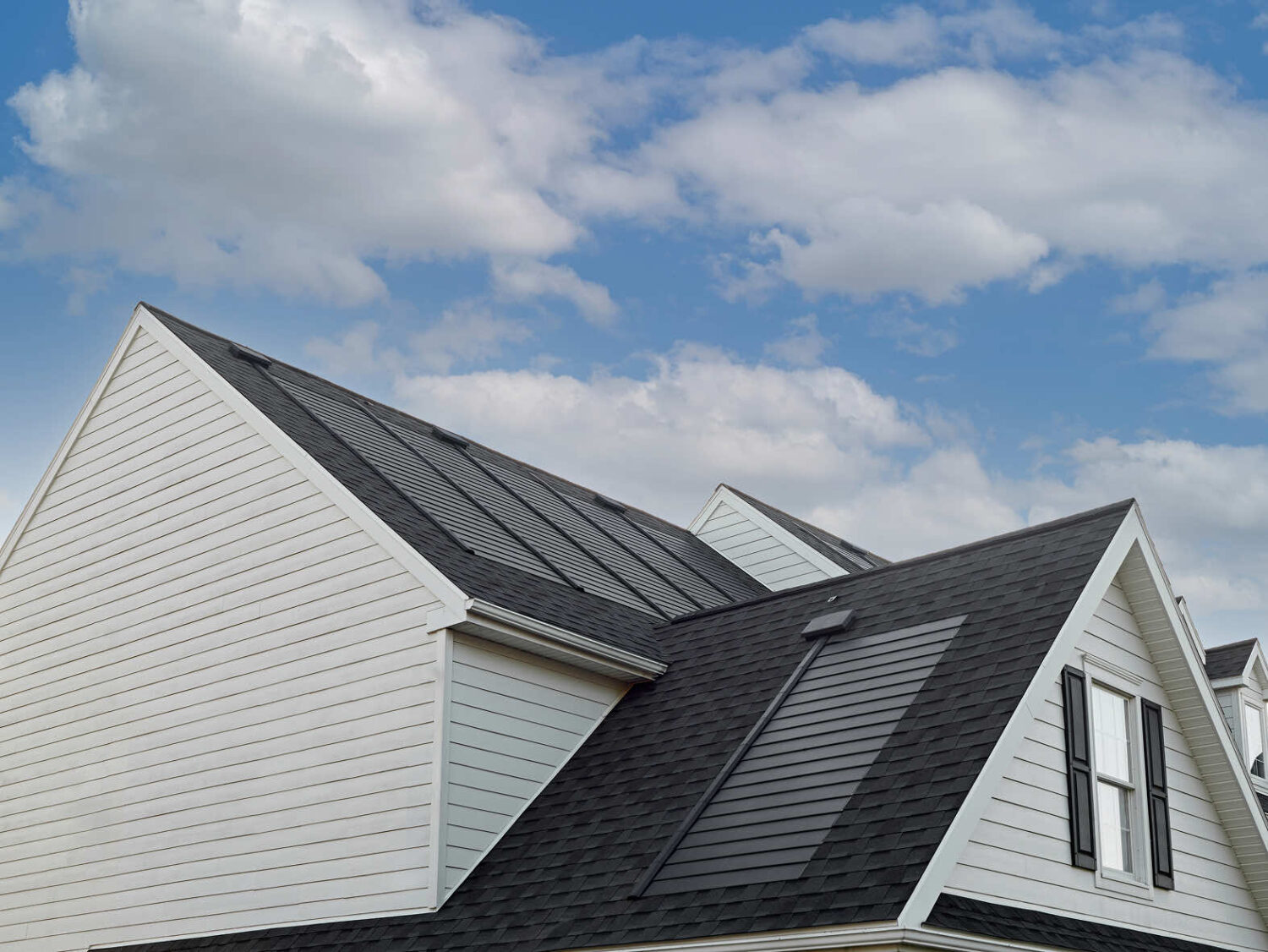 A modern house featuring solar roof shingles under a cloudy sky.