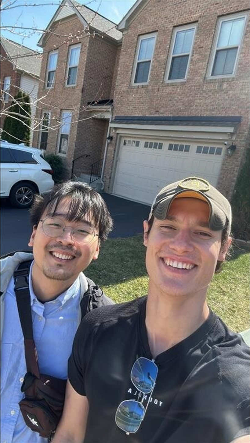Two smiling team members posing in front of a house on a sunny day.