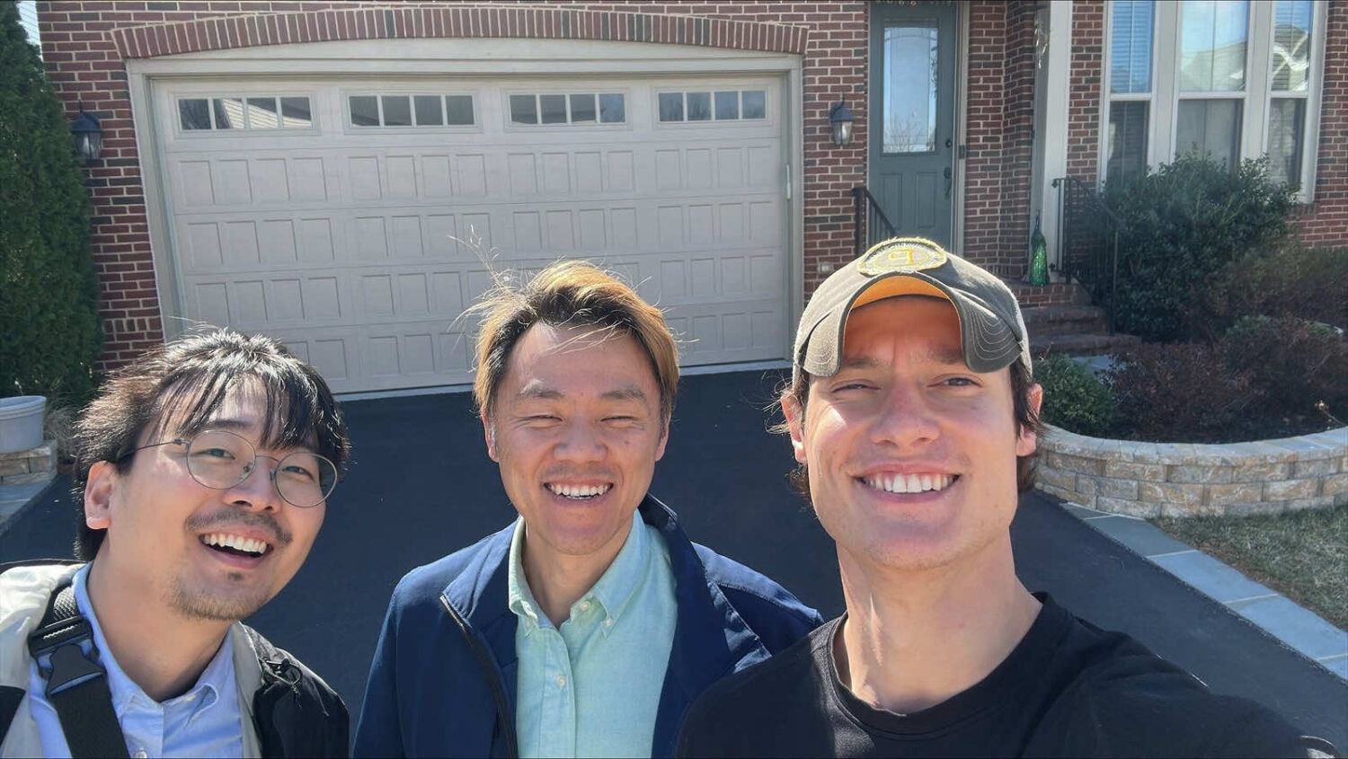 Three team members smiling for a selfie in front of a house with a garage